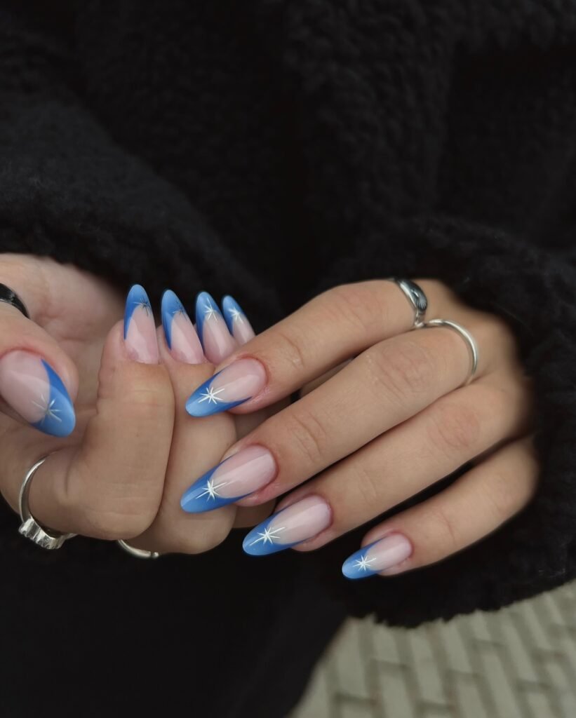 Blue French tips with star accents on glossy nude almond nails.  