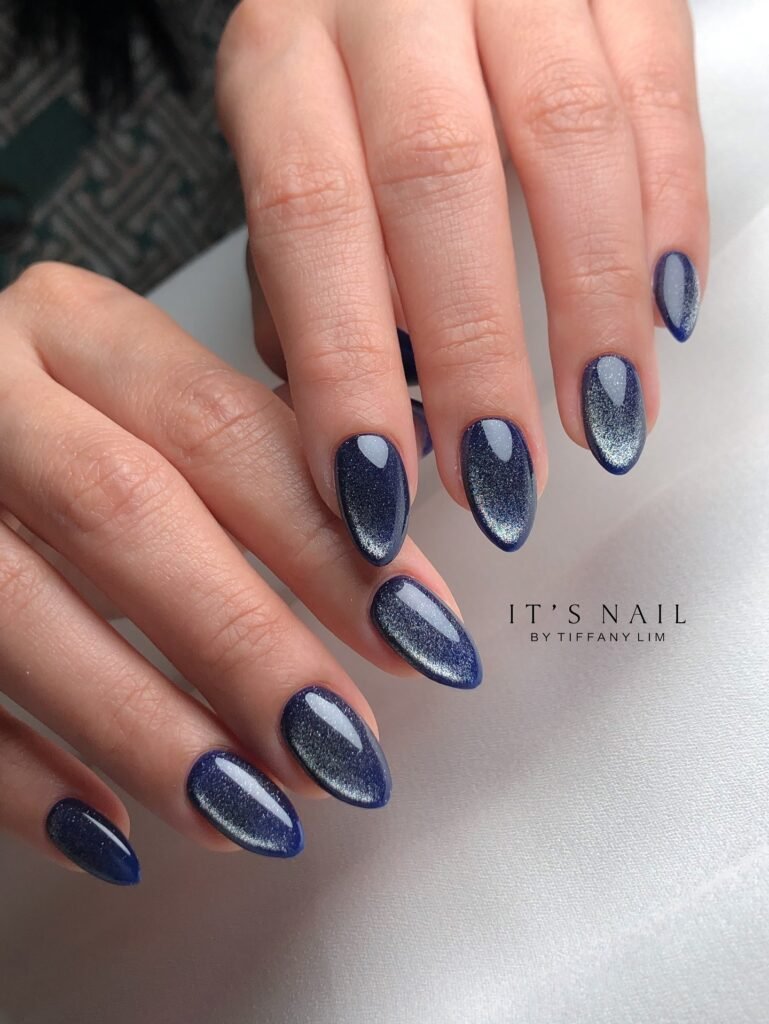 Glossy oval nails with deep navy cat eye shimmer and metallic sheen.  