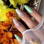 Mint and white almond nails with tiny floral gems and sheer details.