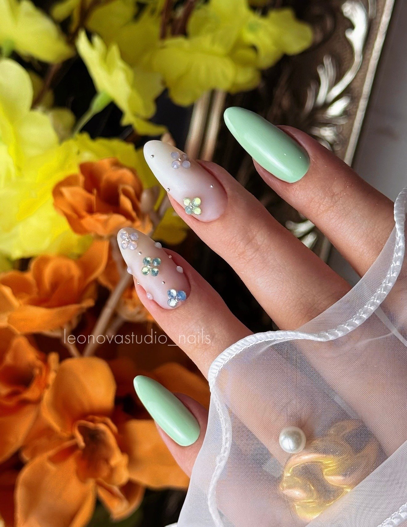 Mint and white almond nails with tiny floral gems and sheer details.
