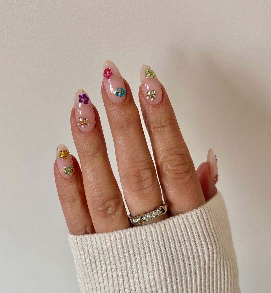 Almond nude nails with tiny multicolor flower gems and glossy finish.  