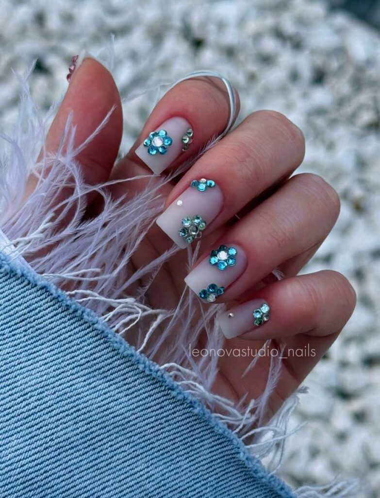 Matte white nails with icy blue rhinestone flowers and soft feather accents.  