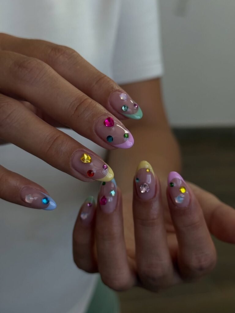 Pastel French tip nails with colorful gem embellishments and glossy highlights  