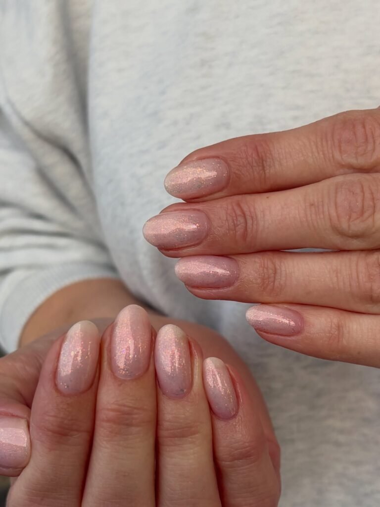 Nude pink oval nails shimmering with fine glitter in soft light.