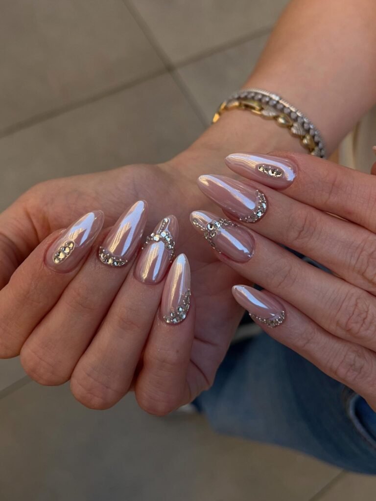 Nude pink almond nails with rhinestone curves and glossy high shine finish.