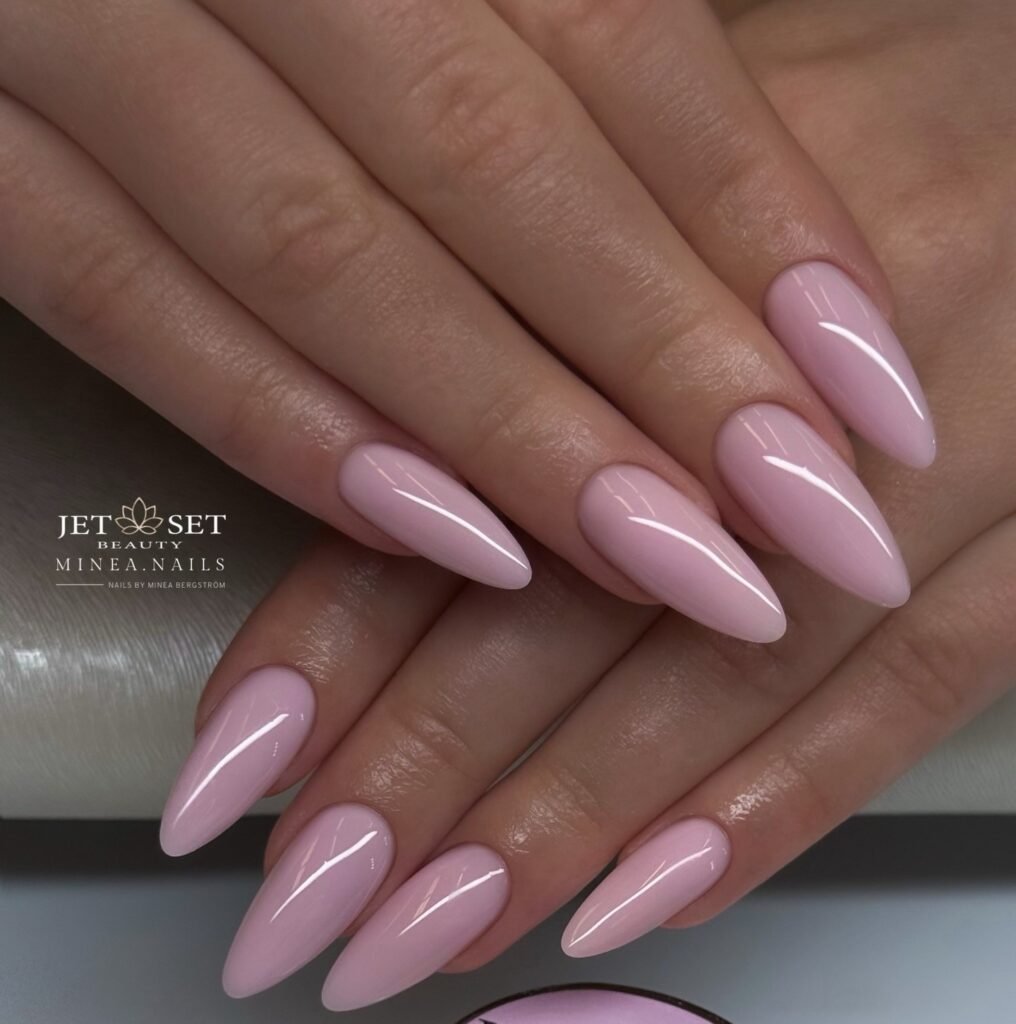 Long glossy pale pink coffin nails posed above a Jet Set Beauty product jar.