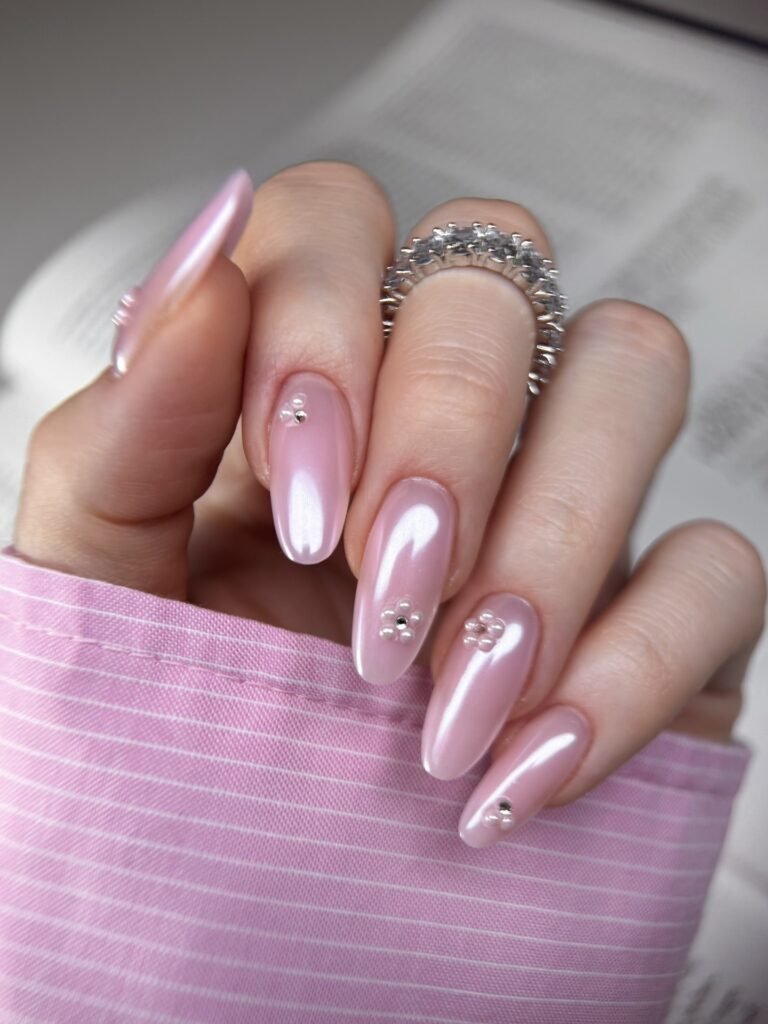 Glossy blush pink almond nails with floral rhinestones and silver rings.