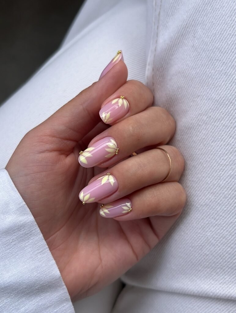 Pink almond nails with pale yellow floral accents and tiny gold beads.