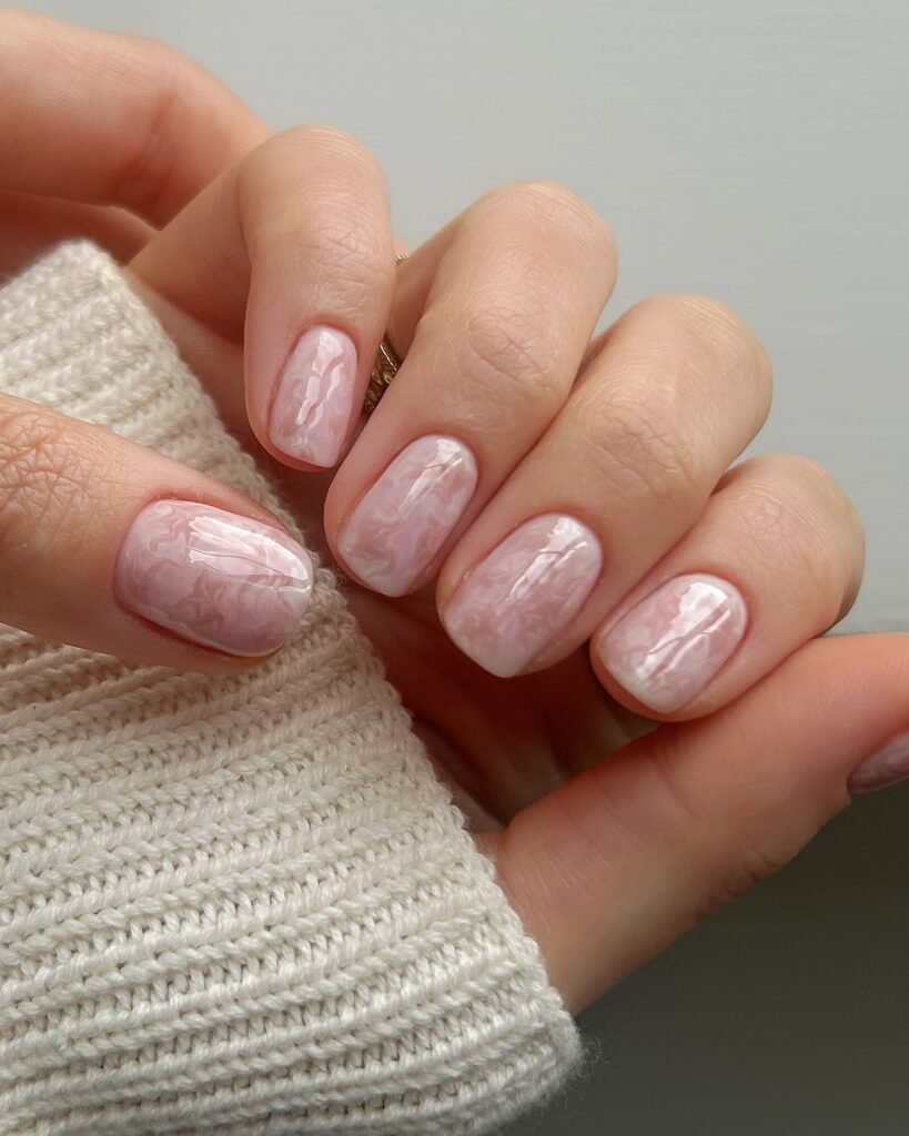 Short square nails with cloudy white marbling over a sheer pink base.