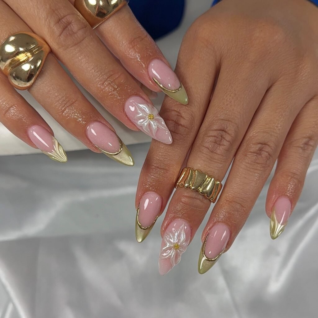 Soft pink almond nails with metallic gold tips and floral accents.  