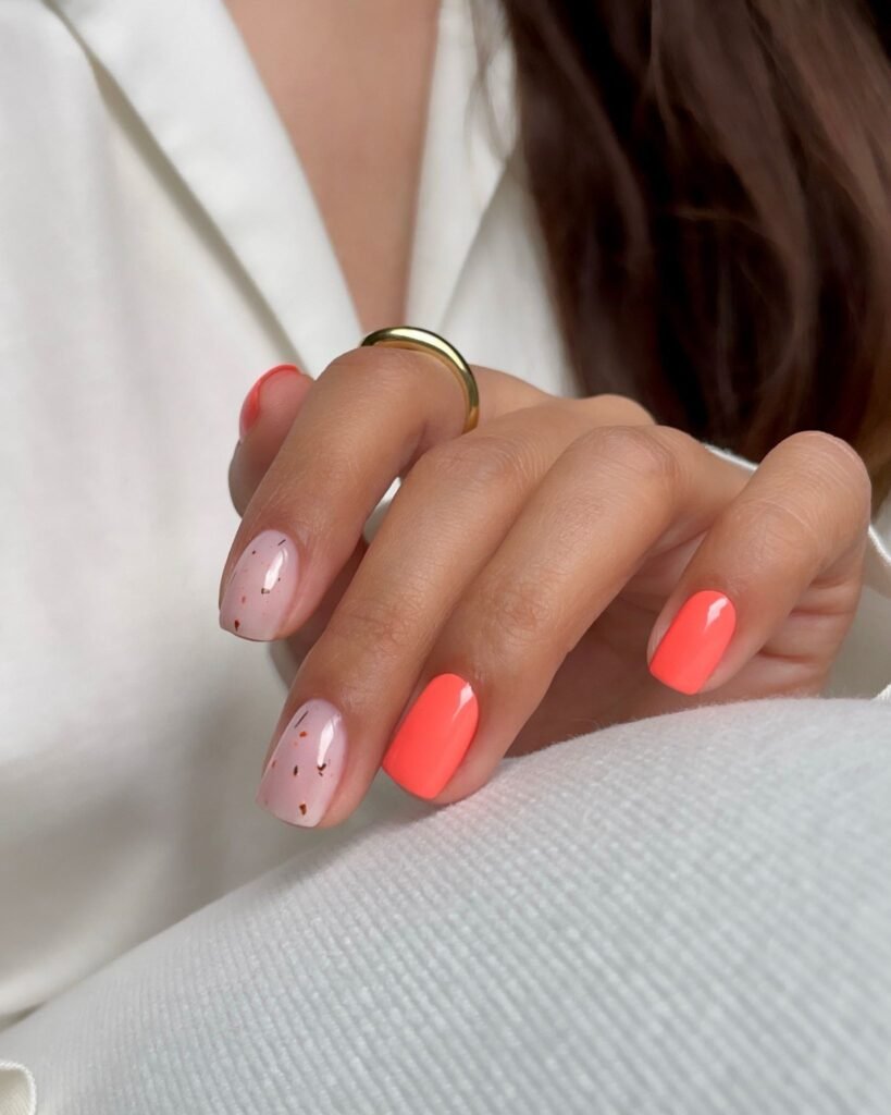 Hand with coral solid nails and pale pink speckled accent nails.  