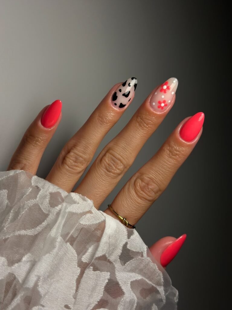 Hand with coral nails, black cow print, and tiny floral accent details.