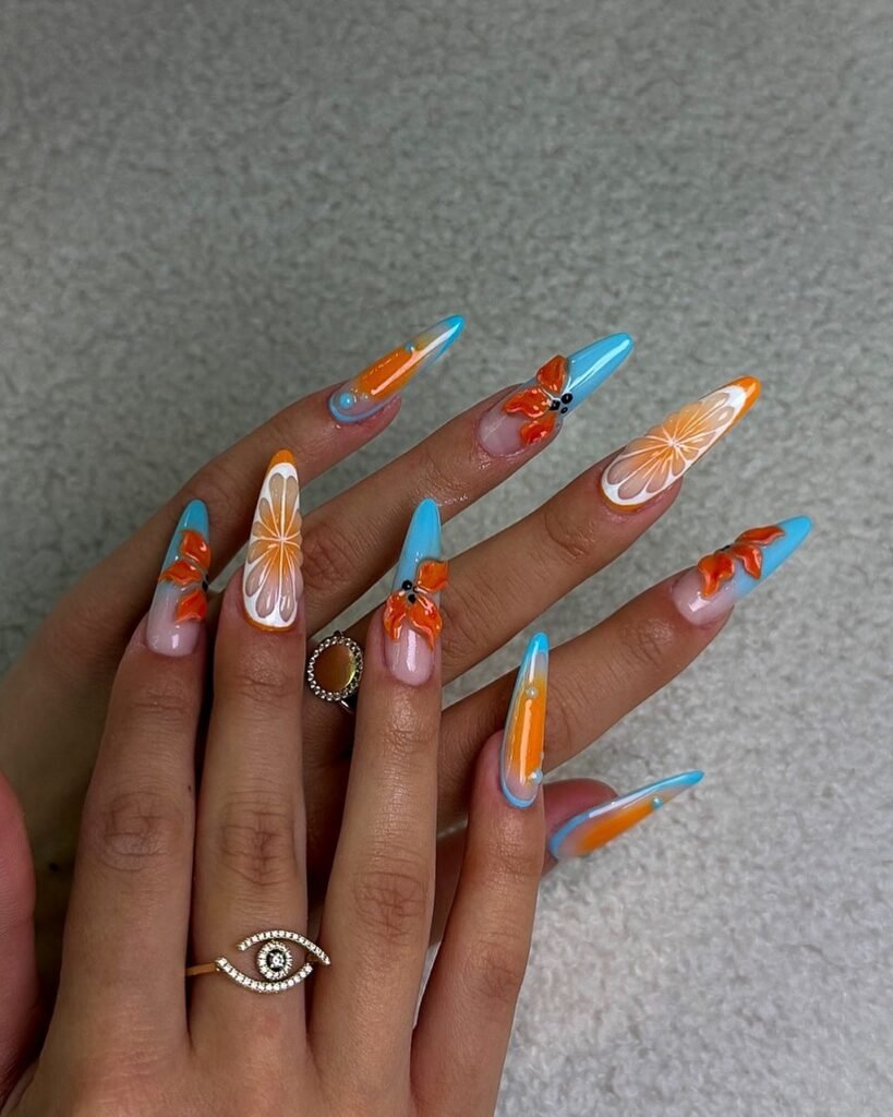 Long pointed nails with blue and orange floral designs, glossy finishes, and a bright tropical color palette.