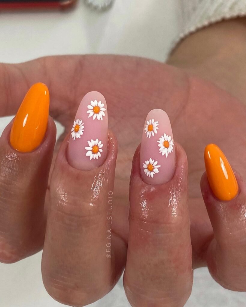 Nude and orange nails with small white daisy flowers and a clean, cheerful minimalist design.