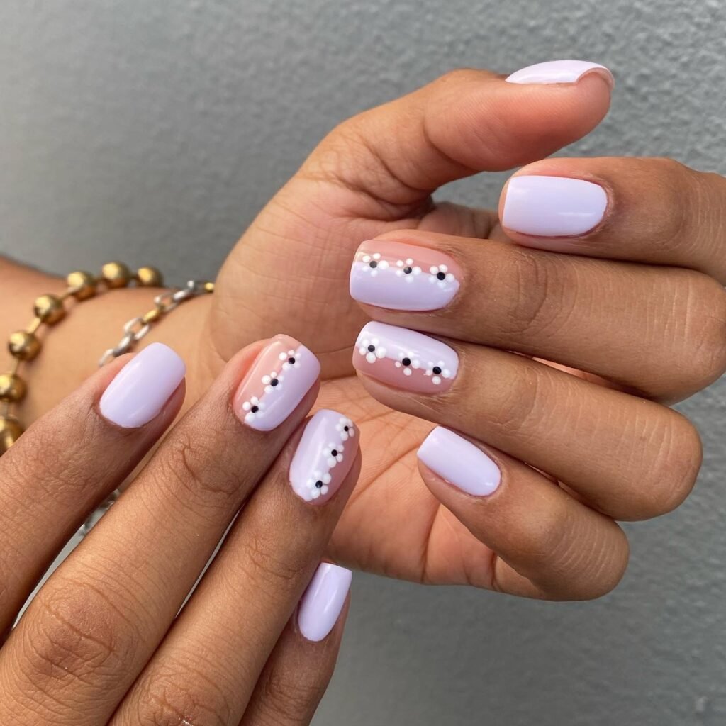 Short lilac nails featuring dotted floral lines and soft neutral bases.