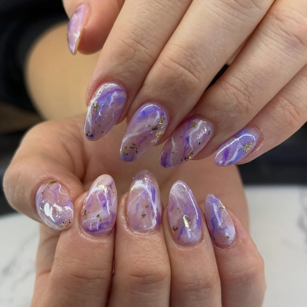Purple marble nails with soft swirls and shimmering gold foil accents.