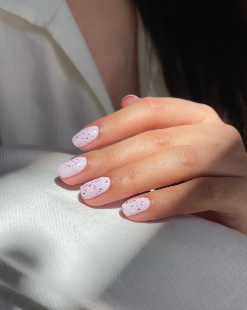 Pastel lilac nails with confetti speckles and a glossy finish.