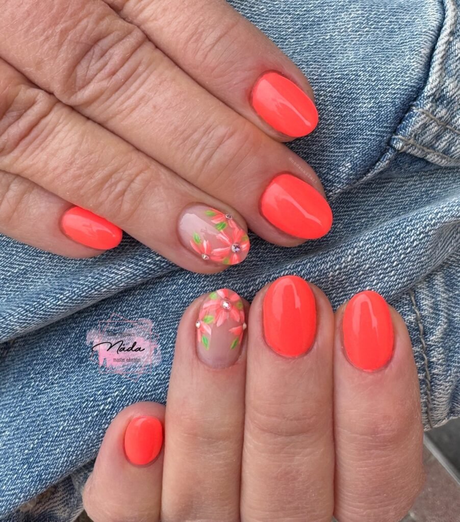 Bright coral nails with floral accent art and rhinestones