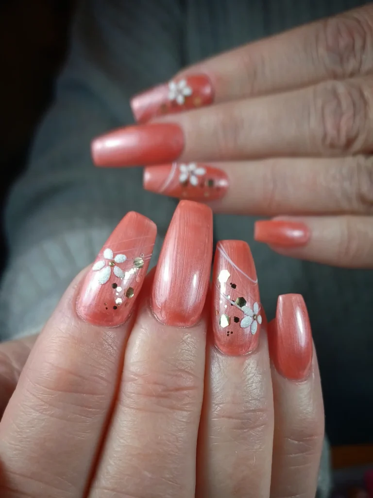 Shimmery coral nails with white flowers and swirl accents